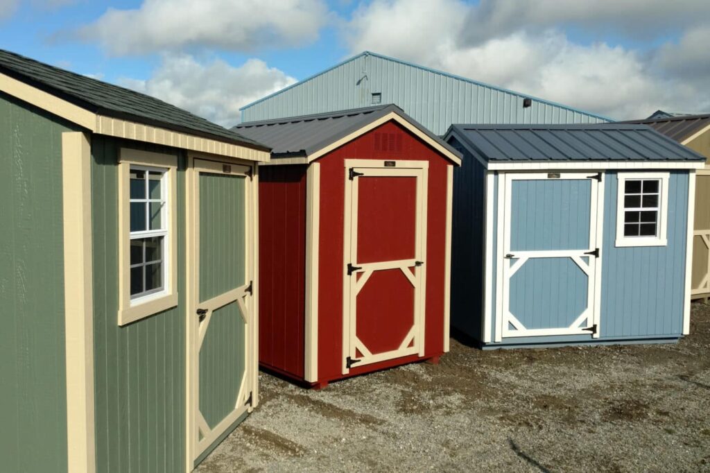A display of small, colorful backyard sheds in the foreground, contrasted with a large blue metal warehouse structure in the background built by Steel City, showcasing the larger scale of Customization and Technical  Factory Sheds engineered by Industrial Shed Manufacturers in Pakistan