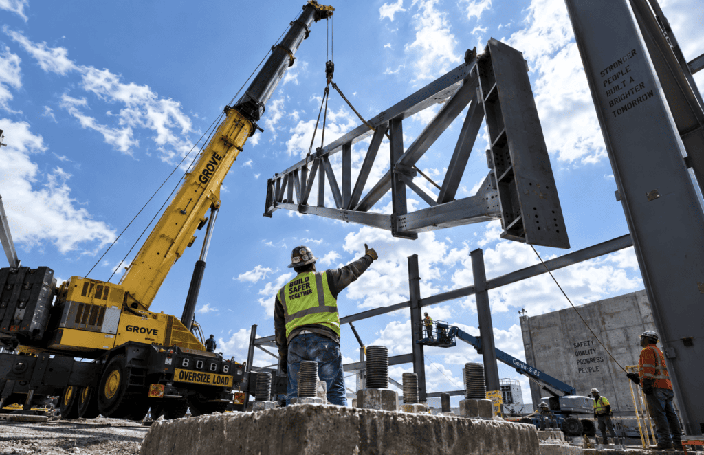 Mobile crane lifting a primary steel frame onto concrete foundations.